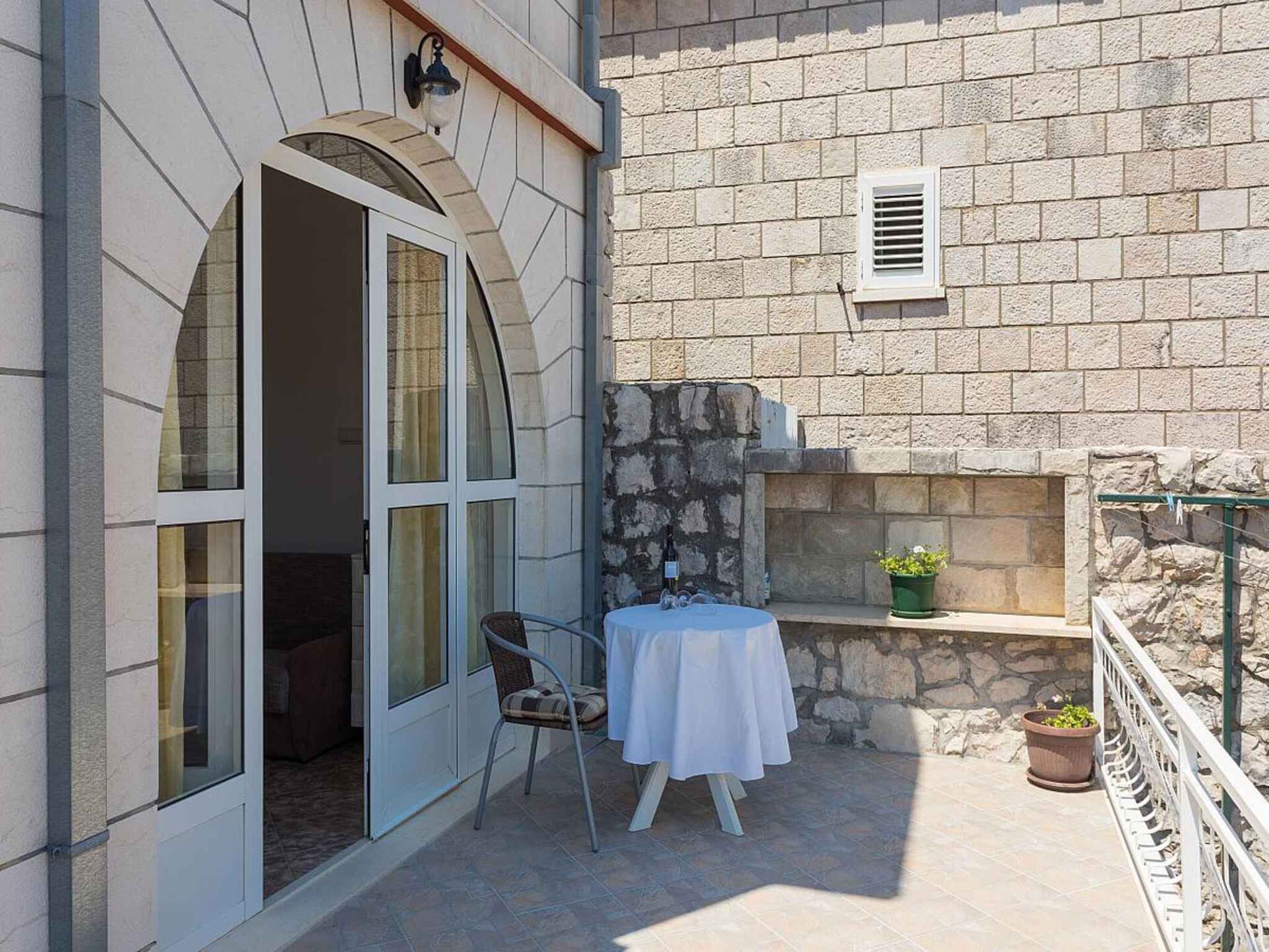 A small outdoor seating area with a table and chairs, a potted plant, and a stone wall.