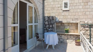 A small outdoor seating area with a table and chairs, a potted plant, and a stone wall.