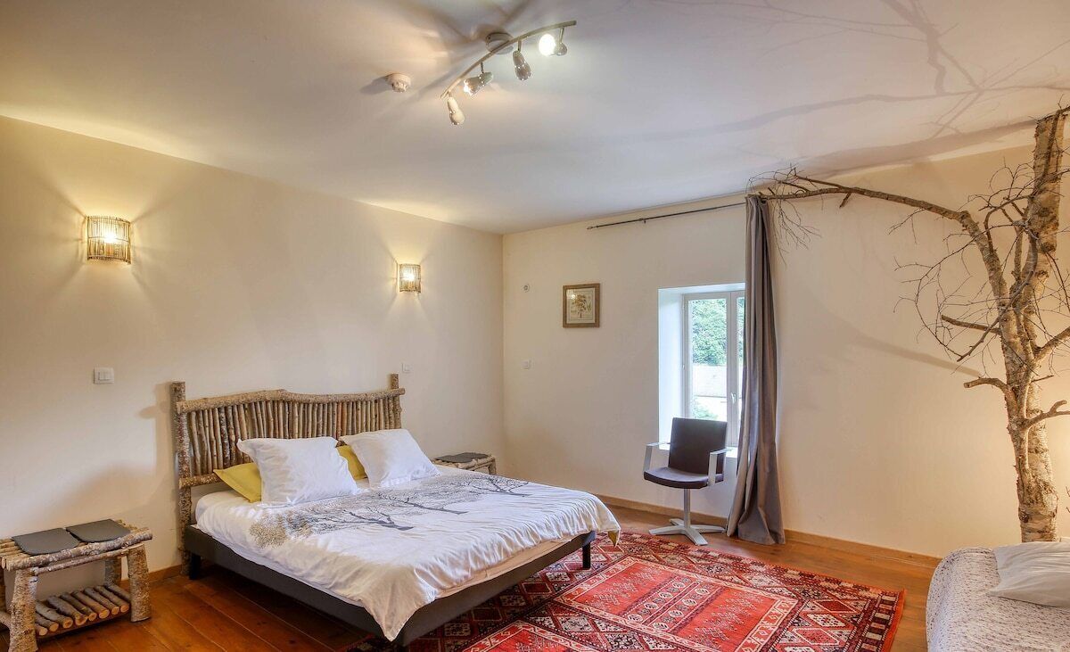 A bedroom with a bed, bedside table, lamp, chair, and a large window.