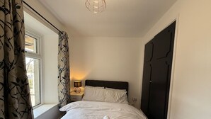 A neatly made bed with a rolled towel, a bedside lamp, and a window with curtains. - Hideaway 4-Bed House in Bridgend" (Bridgend County Borough)