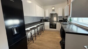 A modern kitchen with white cabinets, a black refrigerator, a stainless steel range hood, and a window providing natural light. - Hideaway 4-Bed House in Bridgend" (Bridgend County Borough)