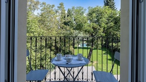 Un balcon avec une table dressée pour deux personnes, donnant sur un jardin bien entretenu.