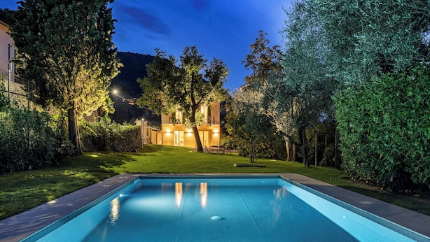 Une piscine à l’eau d’un bleu limpide, entourée d’une pelouse bien entretenue et d’arbres.