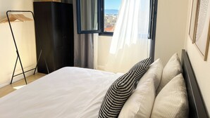 Une chambre à coucher avec un lit, une armoire, une fenêtre avec des rideaux et une vue sur la ville.