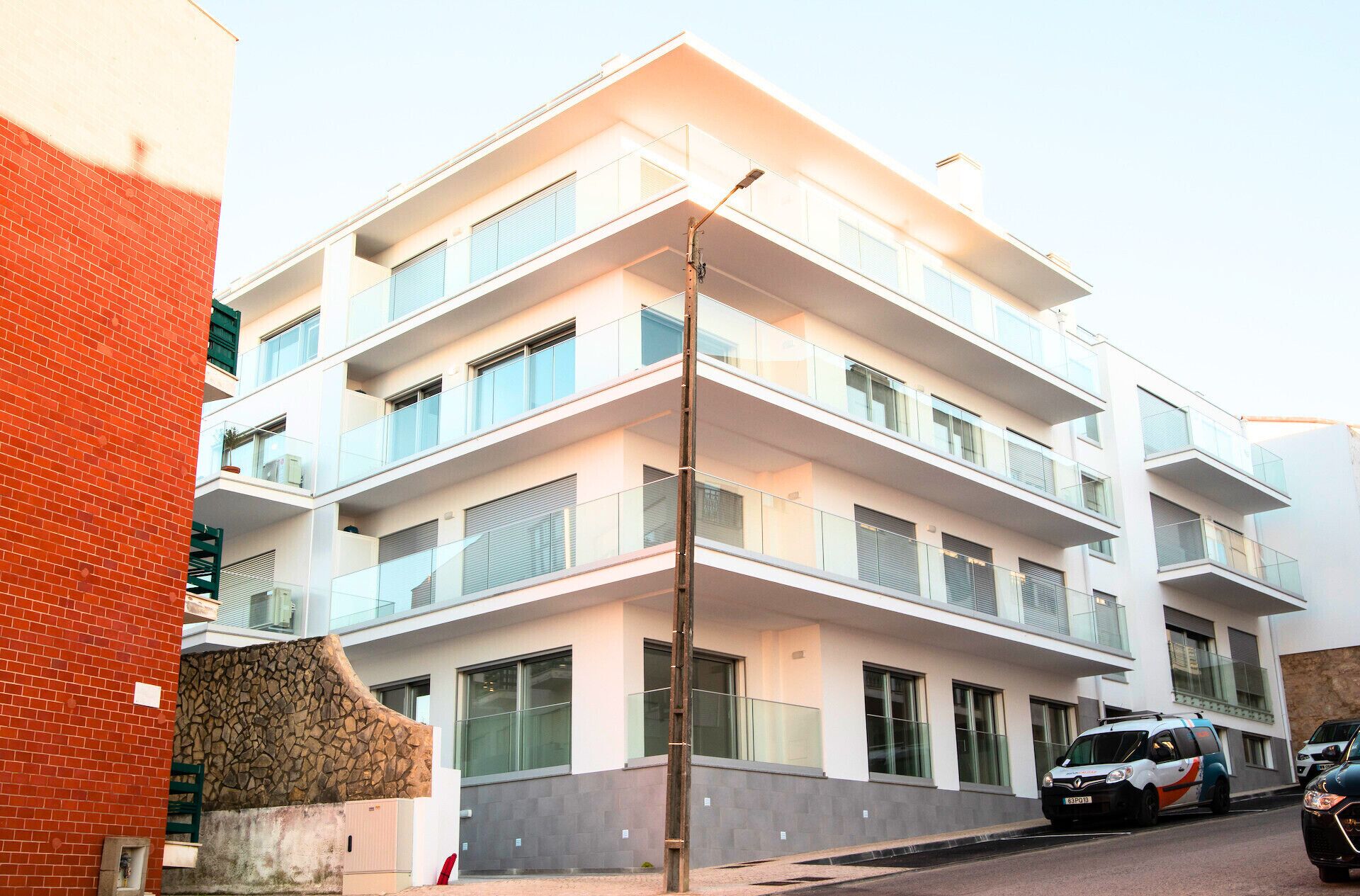 Un edificio residencial de varios pisos con balcones, un muro de piedra y un automóvil estacionado.