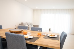 A dining area with a wooden table, chairs, a bowl, glasses of orange juice, and a sofa in the background.