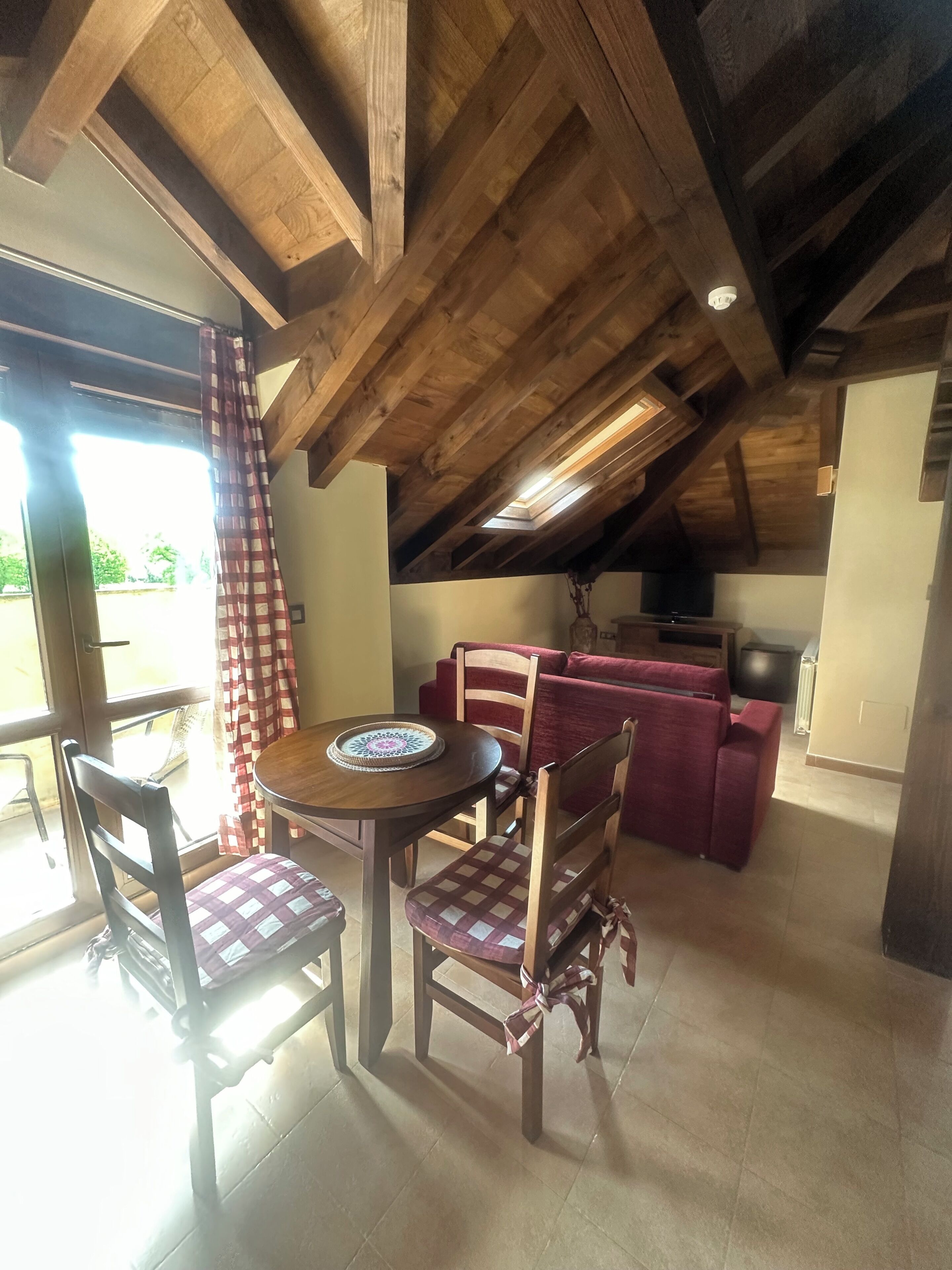 A dining area with a wooden table and chairs, a red sofa, and a ceiling with exposed beams.