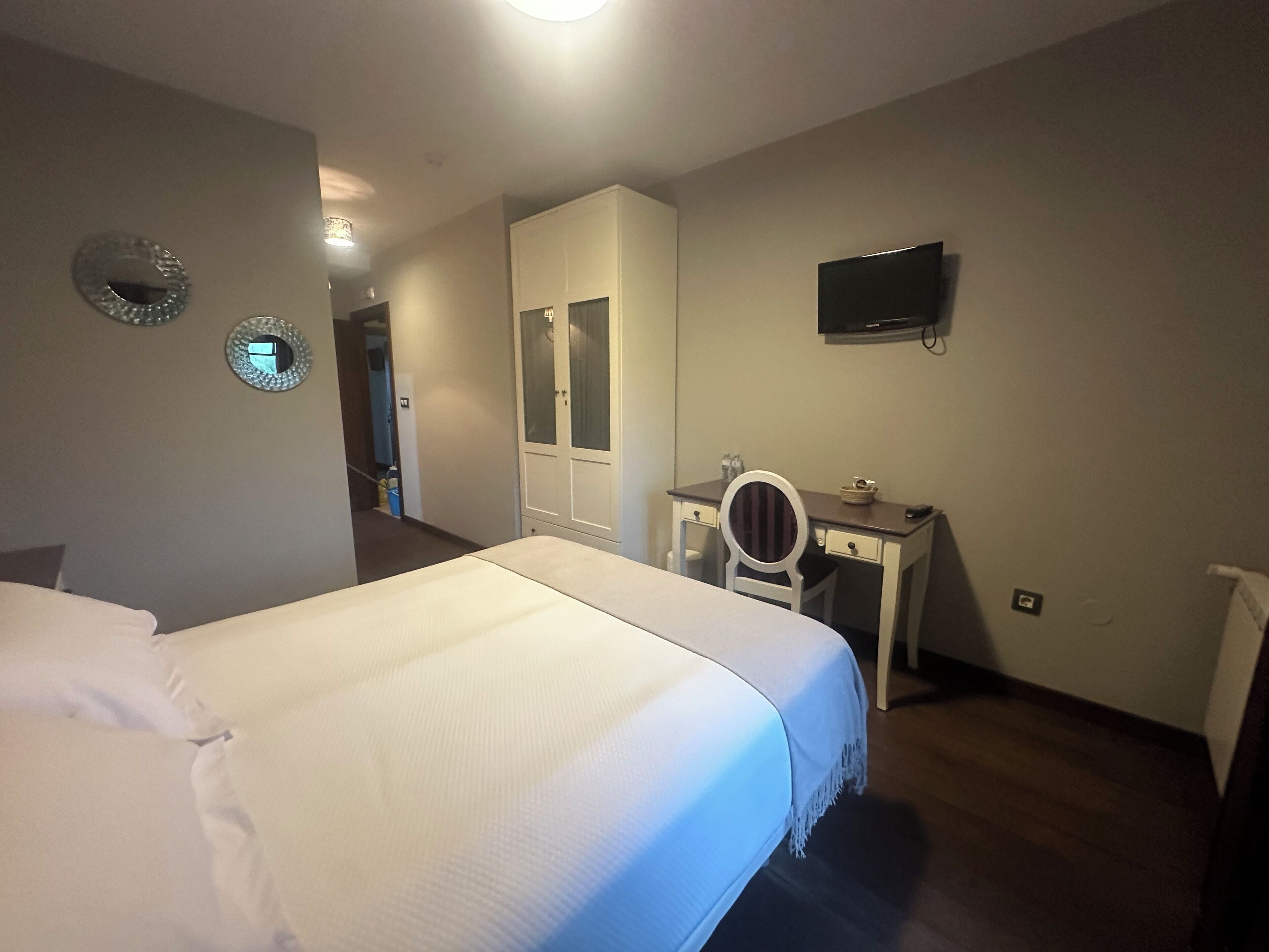 Una habitación de hotel con cama, escritorio, silla, televisor y armario.