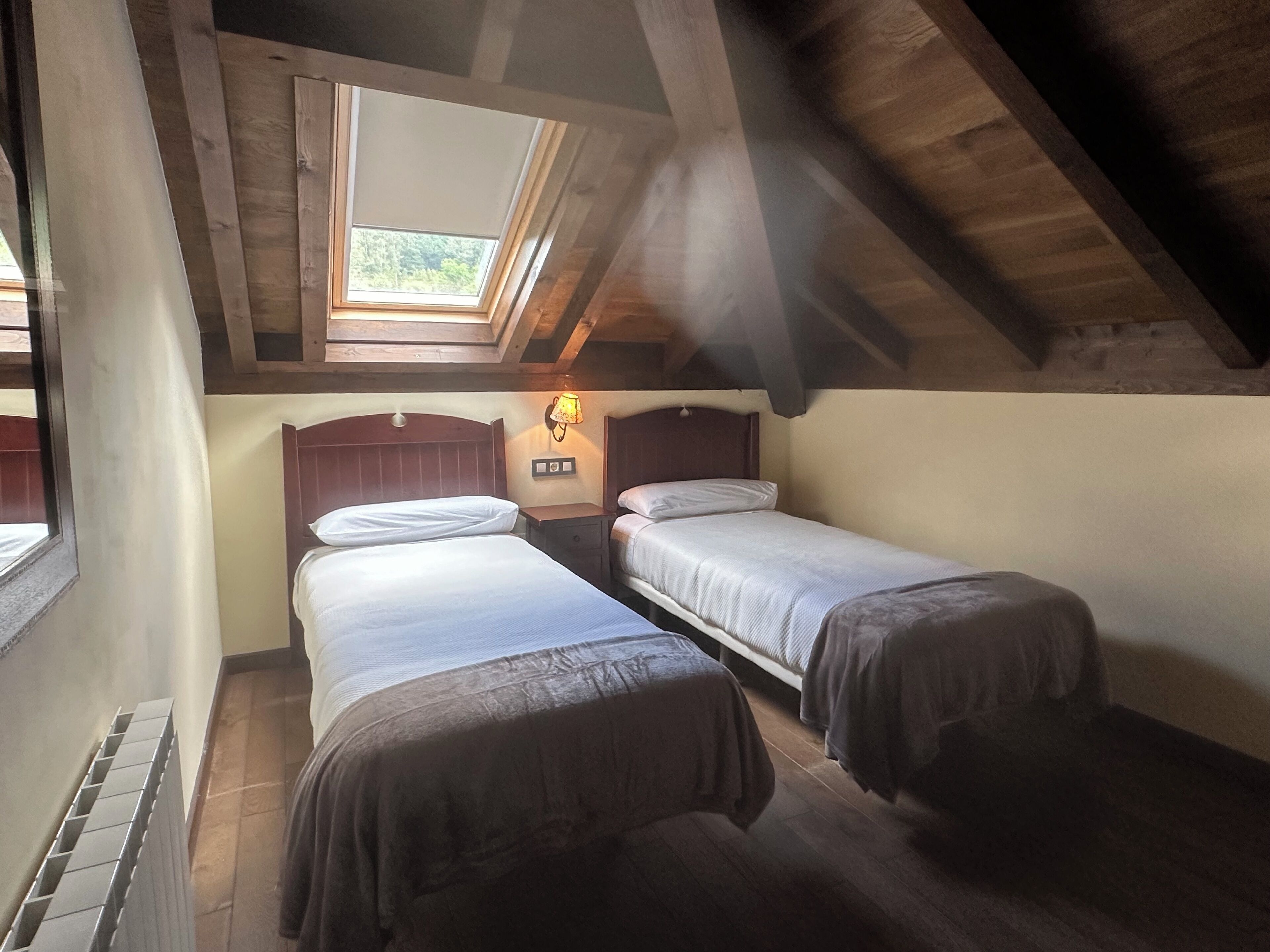 A dormitory room with two beds, a skylight, and a wall-mounted lamp.