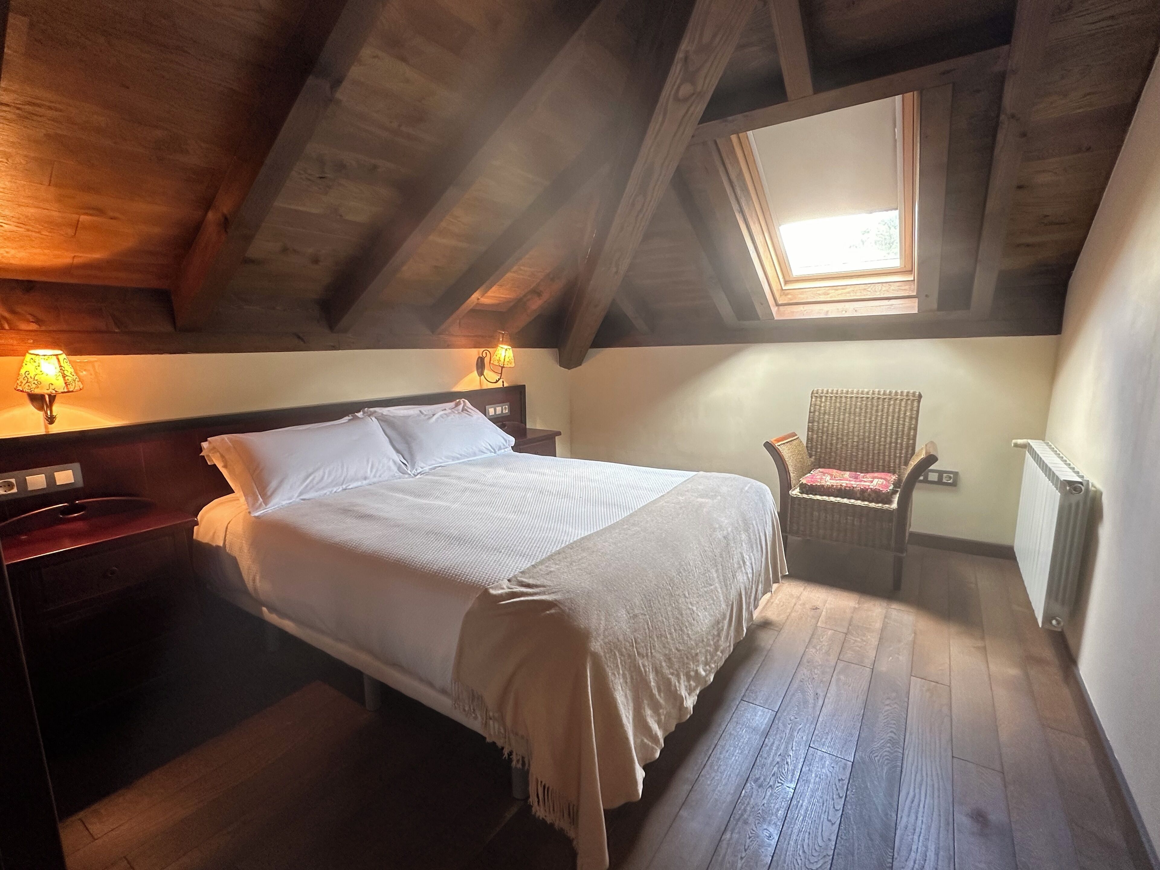 A bedroom with a bed, a chair, a nightstand, a lamp, and a window.