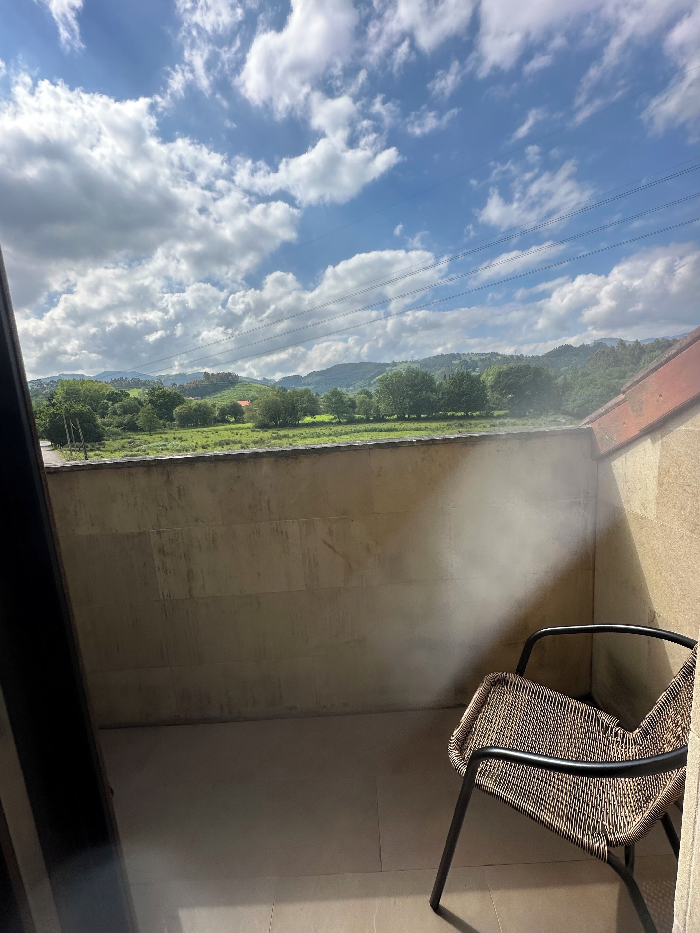 Un balcón con vistas a colinas verdes y un cielo despejado.