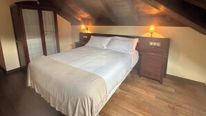 A bedroom with a large bed, wooden headboard, two bedside tables with lamps, and a wardrobe. - Hospedería Rural Santa Cruz (Socobio)