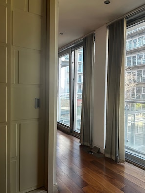 A room with large windows, wooden flooring, and a view of a building outside. - Salford Lux Apartment (Manchester)
