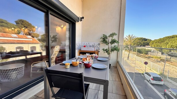 A balcony with a dining table set for two, a chair, and a potted plant.