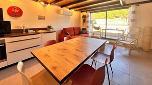 A modern kitchen with a wooden table and red chairs, a red sofa, and a large window with a view of greenery.
