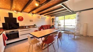 A modern kitchen with a wooden ceiling, a dining area with red chairs, and a large window providing a view of the outdoors.