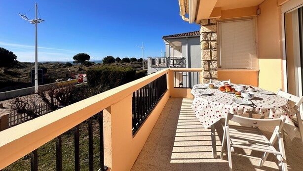 A balcony with a table set for dining, overlooking a scenic landscape with trees and a wind turbine.