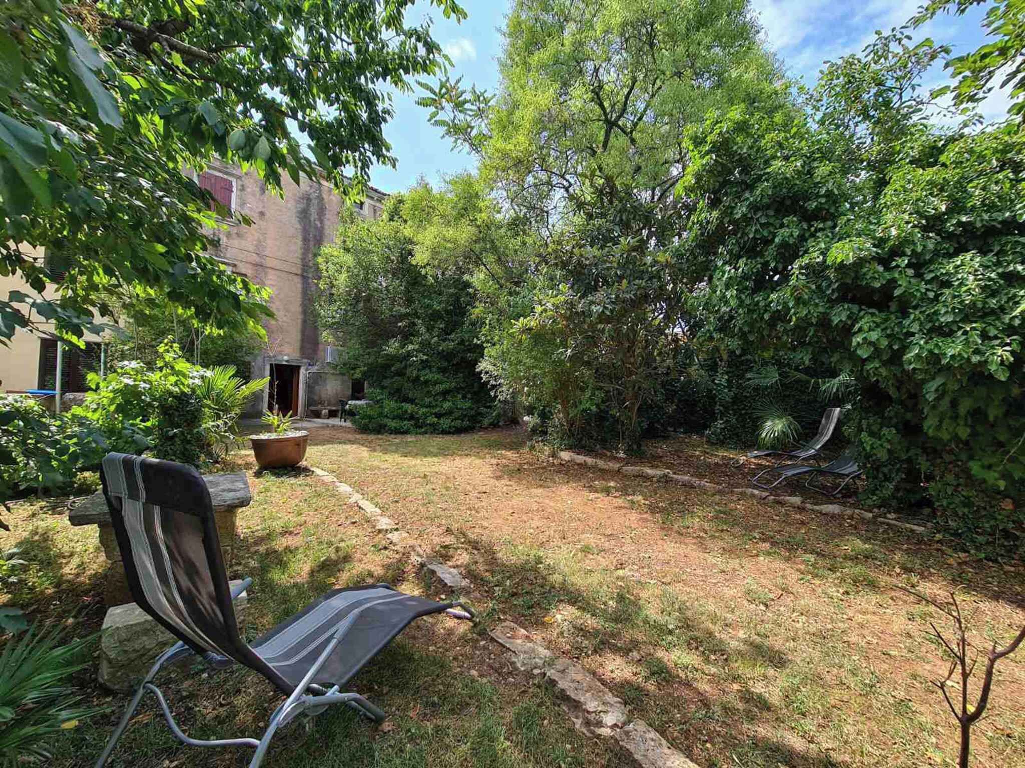 Un patio trasero con césped, una mesa de patio y una silla. Hay árboles y un edificio al fondo.