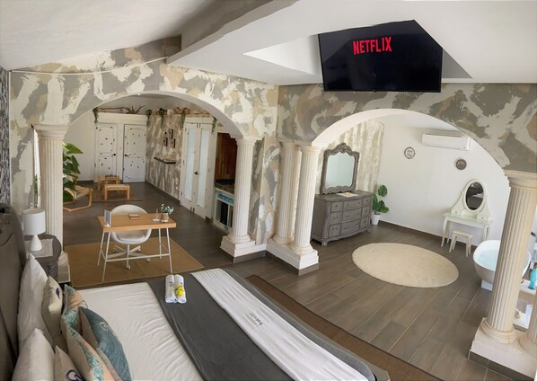 Une chambre d’hôtel avec un grand lit, un bureau avec une chaise, une coiffeuse avec un miroir et un téléviseur fixé au mur.