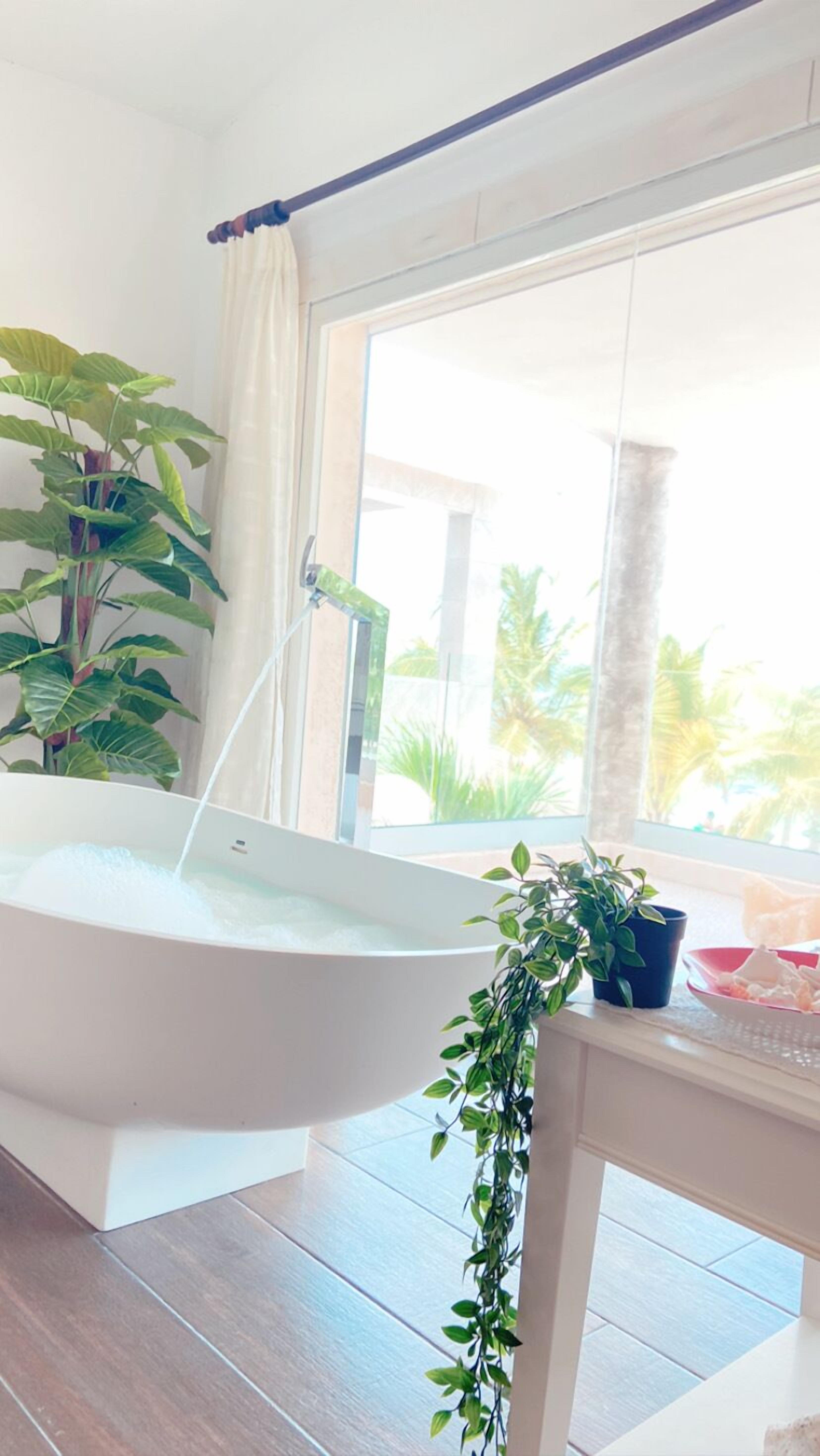 Ein modernes Badezimmer mit einer freistehenden Badewanne, einem großen Fenster mit Blick auf Palmen und einem Blumentopf auf der Fensterbank.