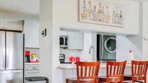 A modern kitchen with stainless steel appliances, a dining area with wooden chairs, and a wall-mounted artwork. - Charming 2-bedroom condo with AC, WiFi in quaint Stuart (Stuart)