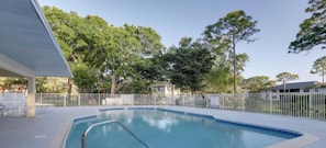 Una piscina con cerca blanca, rodeada de árboles y un edificio.