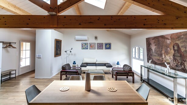 Amplia sala de estar con techo alto y tragaluces, sofá blanco, sillones de cuero, mesa de comedor y un cuadro grande en la pared.