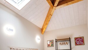 Un dormitorio con techo de madera, tragaluz, cama con ropa de cama blanca, mesita de noche y luces fijadas en la pared.