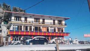 A two-story building with a red and yellow awning, multiple balconies, and parked cars in front. - Hotel Himalaya View (Dehradun)