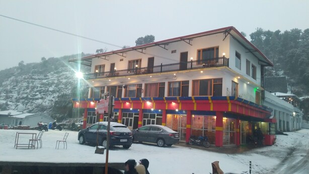A multi-story building with a balcony, a signboard, and parked cars. - Hotel Himalaya View (Dehradun)
