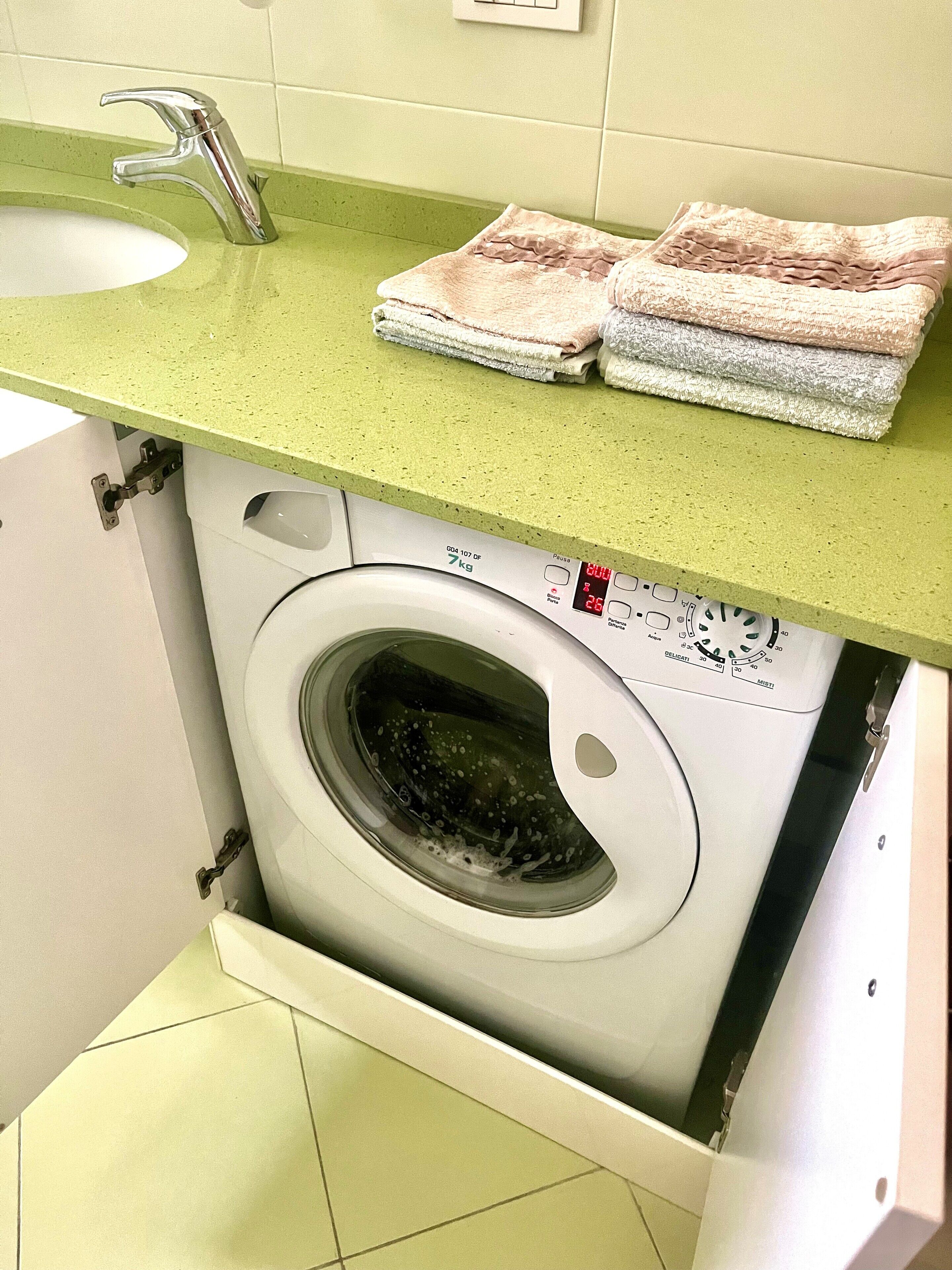 Un área de lavandería compacta con lavadora, lavamanos y encimera con toallas dobladas.