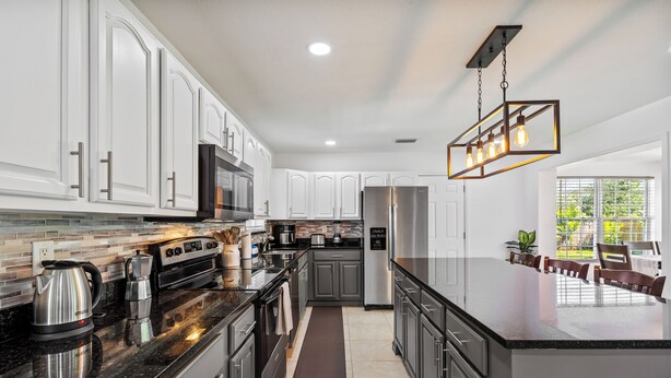 A modern kitchen with white cabinets, stainless steel appliances, and a large island. - Orchard Oasis Retreat (West Palm Beach)
