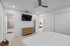 A bedroom with a bed, a wooden dresser, a television, and a ceiling fan. - Orchard Oasis Retreat (West Palm Beach)