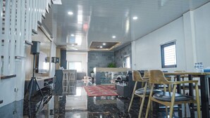 Una sala moderna con piso de mármol negro, un tapete rojo estampado y un sofá. Hay una zona de cocina con barra y taburetes, y un comedor con sillas de madera y una mesa.