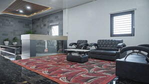 Un amplio salón con un sofá de cuero negro, una mesa de centro y una alfombra estampada. Se observa una recepción al fondo.