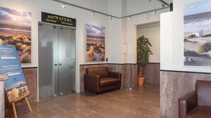 A lobby with a brown leather sofa, a potted plant, and artwork depicting coastal scenes. - Studio in Blankenberge Near the Beach (Blankenberge)