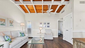 A spacious living room with a wooden ceiling, a glass coffee table, a white sofa, and a grey armchair.