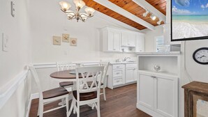A kitchen with white cabinets, a wooden ceiling, and a dining area with white chairs.