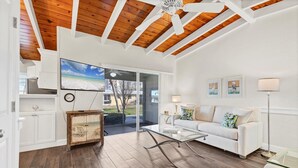 A spacious living room with a wooden ceiling, a glass coffee table, a white sofa, and a view of the outdoors.