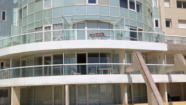 Un bâtiment moderne doté d’une façade incurvée, de grandes fenêtres et d’un balcon avec des chaises.
