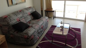 Un salon avec un canapé à motifs, une table basse en verre et un tapis violet.