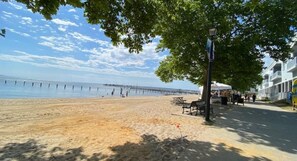 A beach with a pier extending into the water, benches along the shore, and a building with balconies.