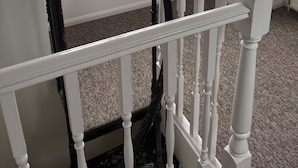 A staircase with white and black balusters leading to a landing with a view of brick buildings through a large window. - Arundel Cottage Retreat (Arundel)