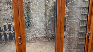 A wooden-framed glass door leading to a backyard with a brick wall and a metal ladder. - Arundel Cottage Retreat (Arundel)