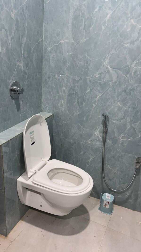 A bathroom with a white toilet, a shower, and a marble wall. - HOTEL SHREE ASHTAVINAYAK GRAND (Mandla)
