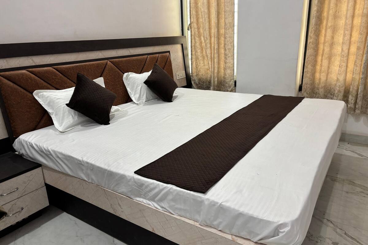 A neatly made bed with white sheets and a brown quilted blanket, a headboard with a geometric pattern, and a bedside table with drawers.