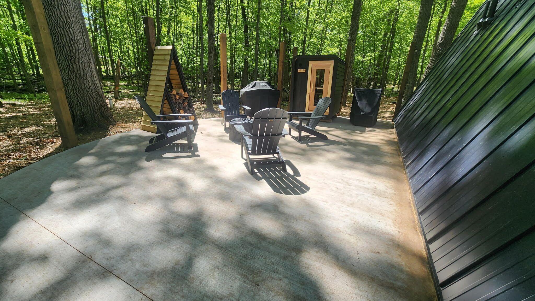 An outdoor patio with Adirondack chairs, a grill, and a small shed.