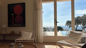 A room with a large sliding glass door leading to a pool, two white chairs, a small table with a tray, and a painting on the wall. - Magnificent villa with panoramic view of the Mediterranean Sea (Le Lavandou)