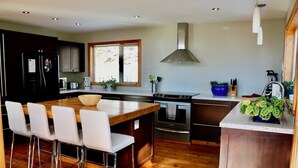Una cocina moderna con una isla central, taburetes de bar, electrodomésticos de acero inoxidable y suelo de madera.
