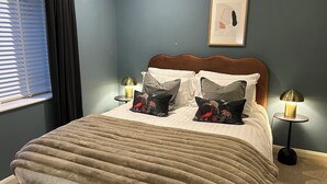 Un lit bien fait, recouvert d’une couverture marron, avec deux lampes de chevet et un tableau encadré accroché au mur.